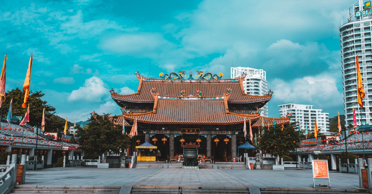 A traditional Asian temple contrasting with modern high-rise buildings under a vibrant sky.